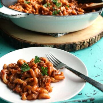 Plate of chili mac with ground beef, elbow macaroni and parsley, with the skillet in the background