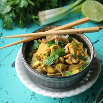 Bowl of chicken curry over broad noodles topped with cashews, fresh herbs and green onions