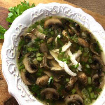 Bowl of chicken marsala soup with sliced mushrooms, shredded rotisserie chicken and green onions in a white scalloped bowl