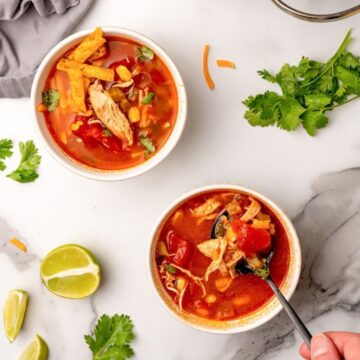 Two bowls of Chili's copycat southwest chicken soup with tortilla strips, cilantro and lime wedges