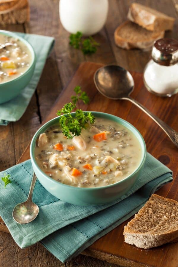 Creamy chicken and wild rice soup with carrots and fresh parsley in a teal bowl on a wooden board with sliced bread