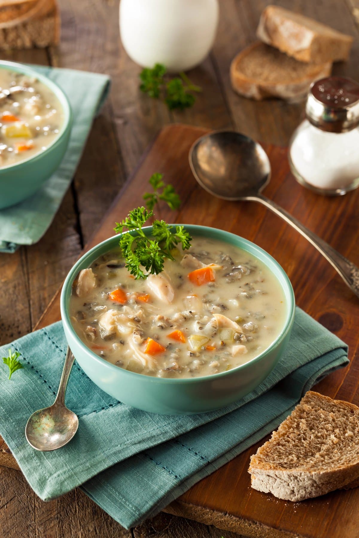 Creamy chicken and wild rice soup with carrots and fresh parsley in a teal bowl on a wooden board with sliced bread