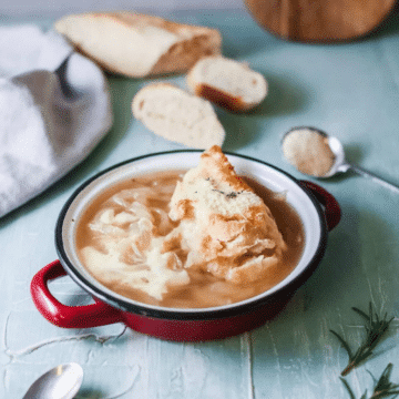 Copycat Panera French onion soup in a red enamel bowl topped with cheesy toasted bread