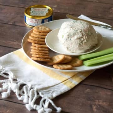 Cream cheese tuna dip shaped into a ball on a white plate with crackers and celery sticks