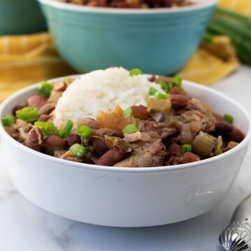 Crockpot Popeyes red beans and rice with shredded ham hock and scallions in a white bowl
