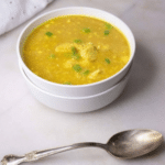 Curried chicken and cauliflower rice soup in a white bowl with a silver spoon