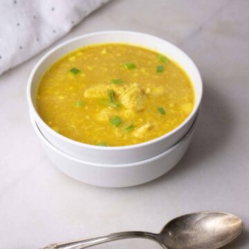 Curried chicken and cauliflower rice soup garnished with sliced green onions in stacked white bowls