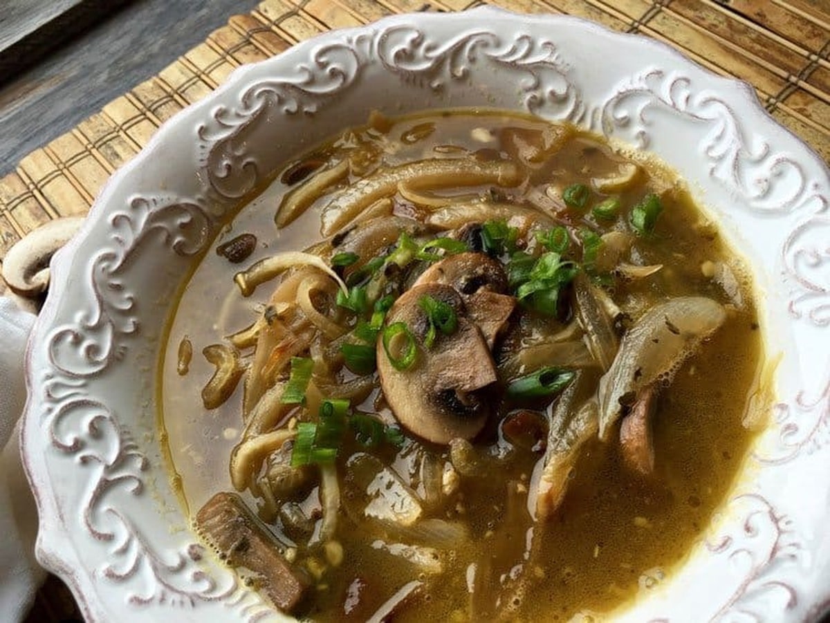 Bowl of daikon noodle soup with sliced mushrooms and green onions on a bamboo mat