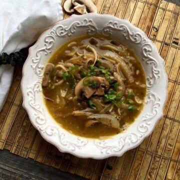 Overhead view of daikon noodle soup with mushrooms, caramelized onions and green onions in a white bowl