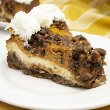 Slice of double layer pumpkin cheesecake with a pecan crust, cheesecake layer, pumpkin pie layer and pecan streusel topped with whipped cream
