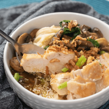 Bowl of easy spicy chicken ramen with sliced chicken, mushrooms, spinach, and crispy onions