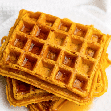 Stack of easy pumpkin waffles drizzled with maple syrup on a white plate