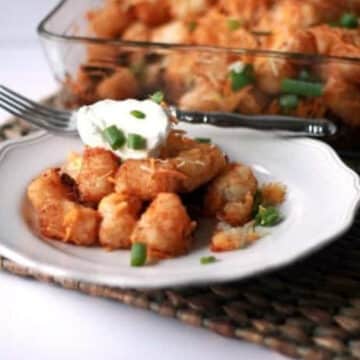 Easy taco tater tot casserole served on a white plate with sour cream and green onions