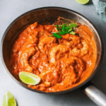 Goan shrimp curry in a skillet with lime wedges and cilantro
