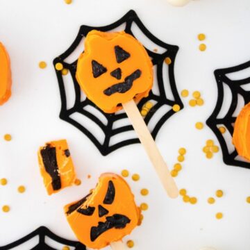 Halloween Pumpkin Cake Pops with jack-o'-lantern faces on black spiderweb coasters