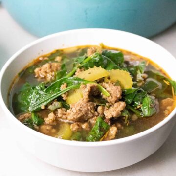 Bowl of keto sausage soup with spinach and celery in front of a teal Dutch oven