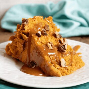 Slice of layered pumpkin cake with pumpkin ganache filling, caramel sauce, and chopped pecans on a white plate