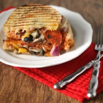 Loaded pizza grilled cheese sandwich stuffed with pepperoni, mushrooms, olives and peppers on a white plate