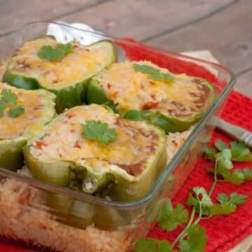 Mexican rice with cheesy stuffed pepper halves in a glass baking dish with fresh cilantro