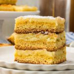 Three squares of Neiman Marcus cake stacked on a white plate, dusted with powdered sugar