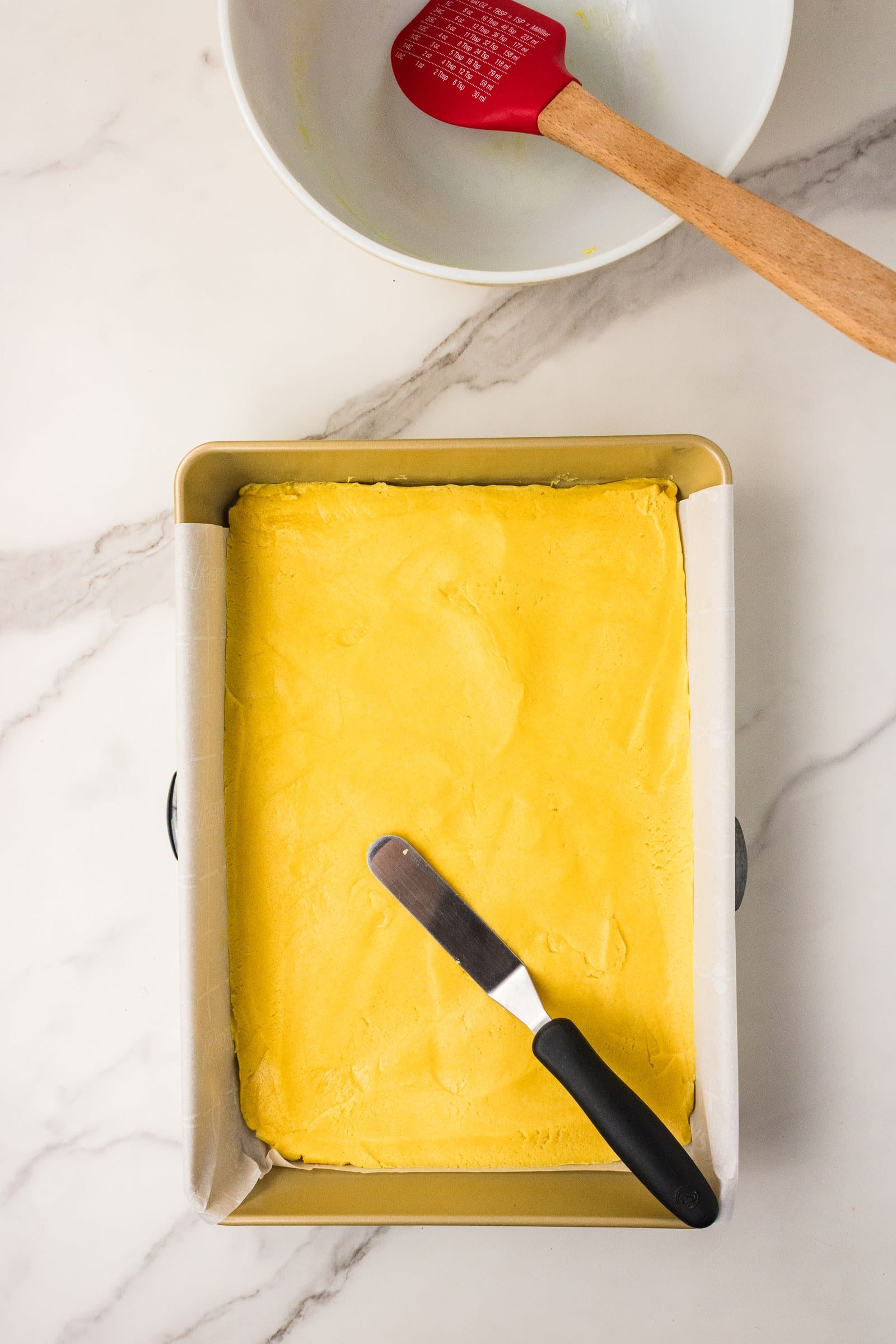 Yellow cake mix crust pressed into a parchment-lined 9x13 baking pan with an offset spatula