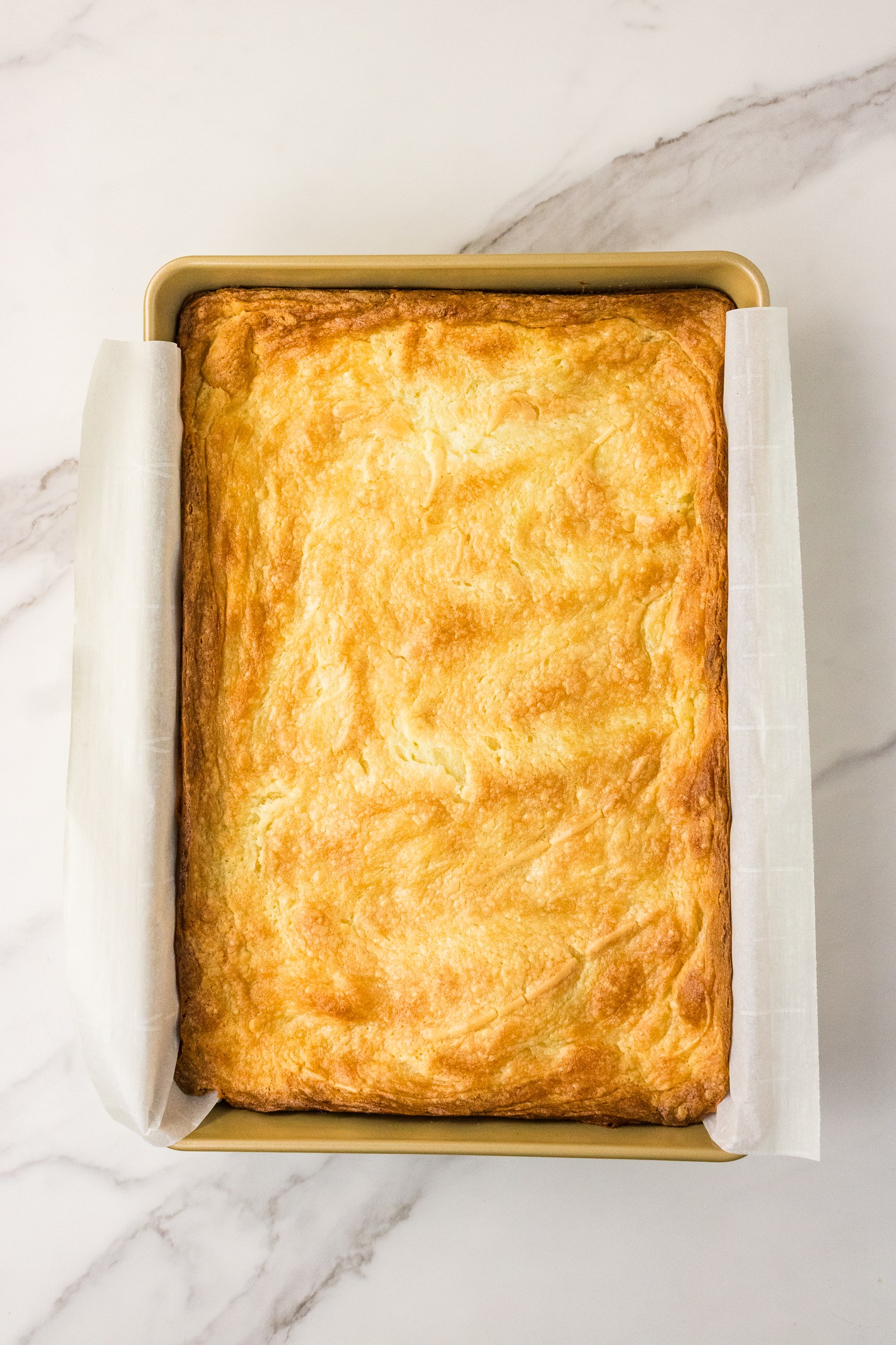 Baked Neiman Marcus cake with a golden, crackly top in a parchment-lined pan