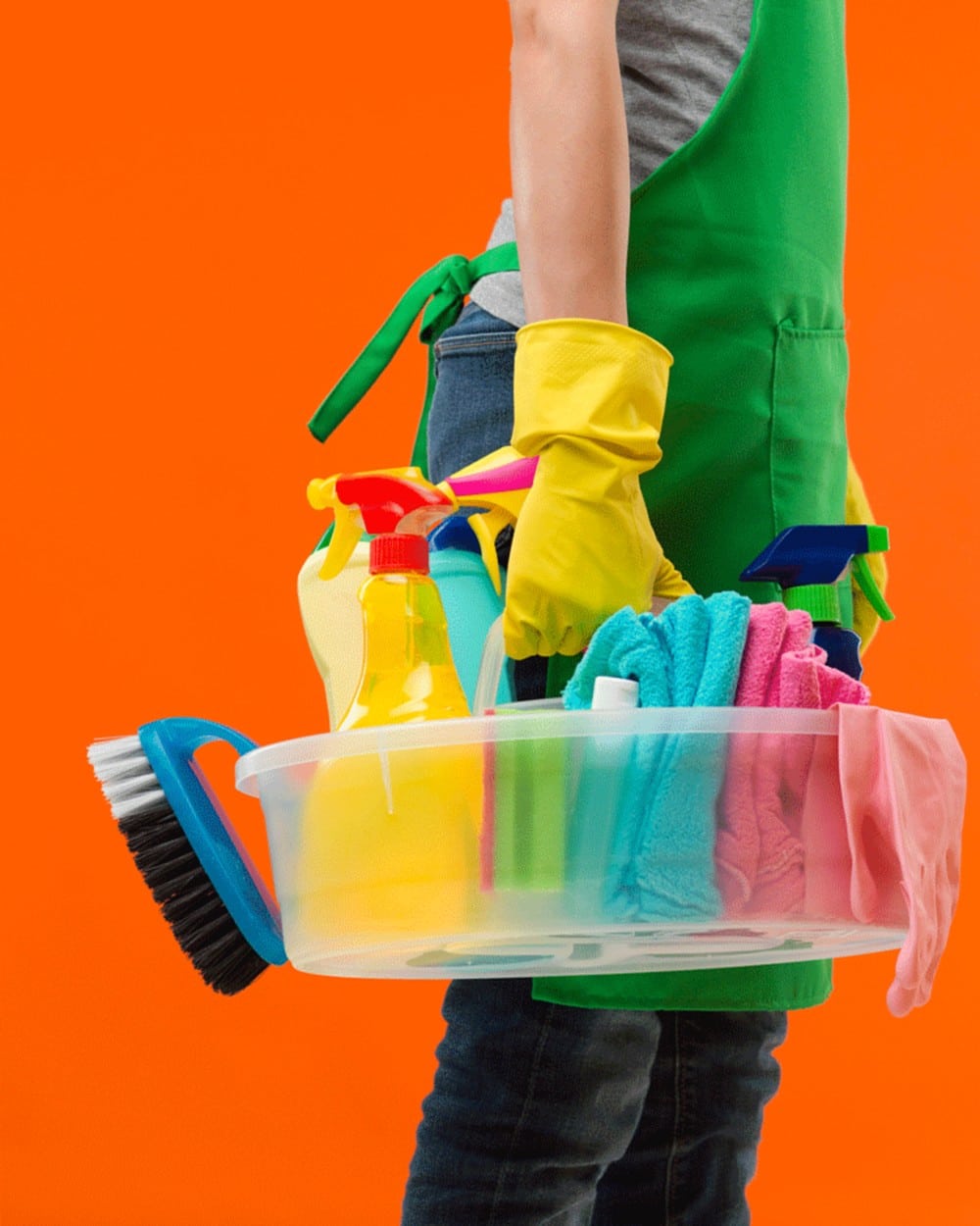 Cleaning caddy filled with spray bottles, microfiber cloths and a scrub brush carried by a person in yellow rubber gloves