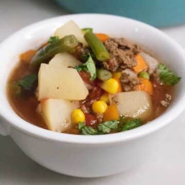 Poor Man's Soup with ground beef, potatoes and mixed vegetables in a white bowl