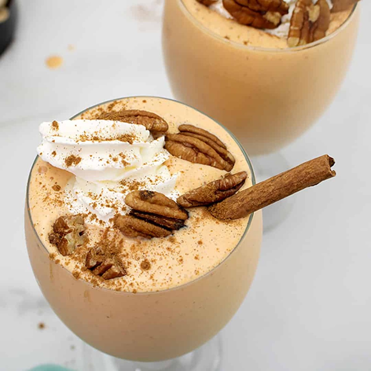 Overhead view of pumpkin cheesecake milkshakes topped with whipped cream, pecans and cinnamon sticks