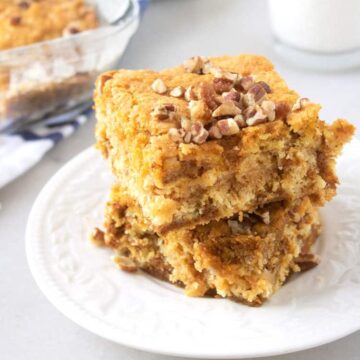 Two squares of pumpkin dump cake topped with chopped pecans stacked on a white plate