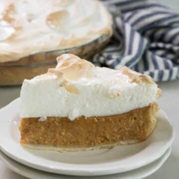 Slice of pumpkin meringue pie with toasted meringue on a white plate