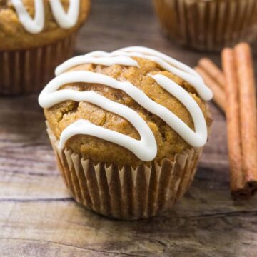 Pumpkin muffin drizzled with cream cheese glaze on a wooden table next to cinnamon sticks