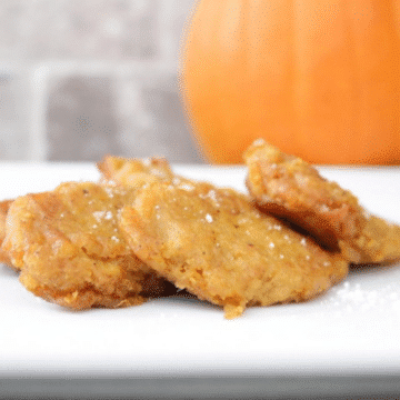 Golden homemade pumpkin patties dusted with powdered sugar on a white plate with a pumpkin in the background