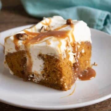 Slice of pumpkin poke cake with cream cheese whipped topping, caramel drizzle, and pecans on a white plate