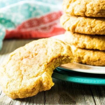 Pumpkin snickerdoodle with a bite taken out in front of a stack of cinnamon-sugar cookies
