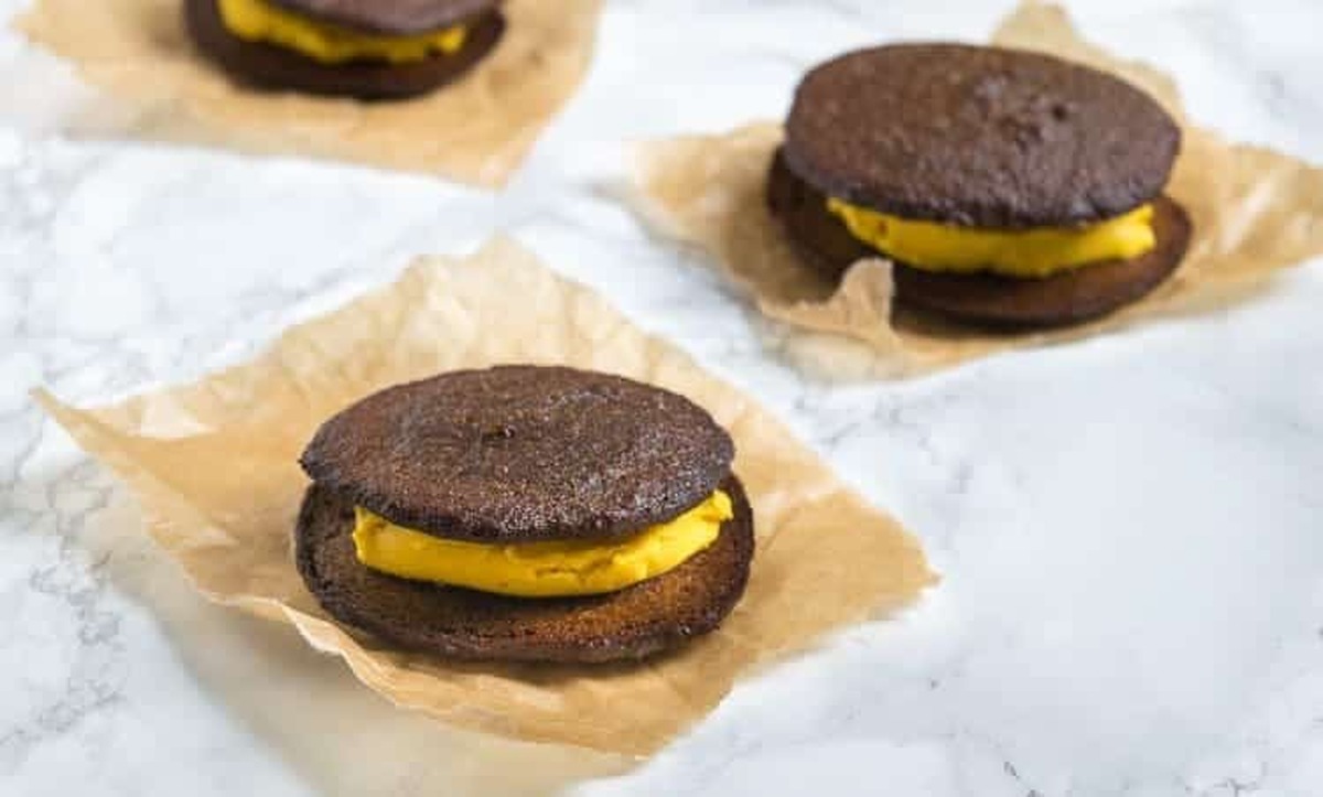 Pumpkin whoopie pies filled with pumpkin cream on squares of parchment paper on a marble counter
