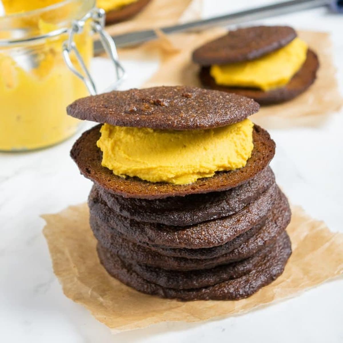 Stack of pumpkin whoopie pies with pumpkin cream filling on parchment paper, with a jar of pumpkin cream behind