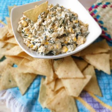 Roasted poblano pepper dip with corn in a white bowl surrounded by tortilla chips