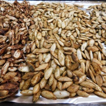 Maple, Indian spiced, and dill and vinegar roasted pumpkin seeds side by side on a foil-lined baking sheet
