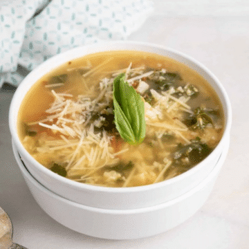 Roasted tomato and cauliflower rice soup topped with shredded Parmesan and fresh basil in a white bowl