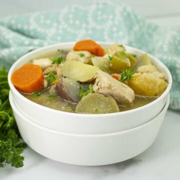 Slow cooker chicken stew with carrots, potatoes and celery in a white bowl with fresh parsley