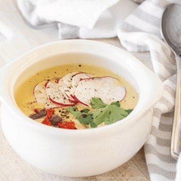 Spicy creamy chicken poblano soup in a white bowl topped with sliced radishes, tortilla strips and cilantro