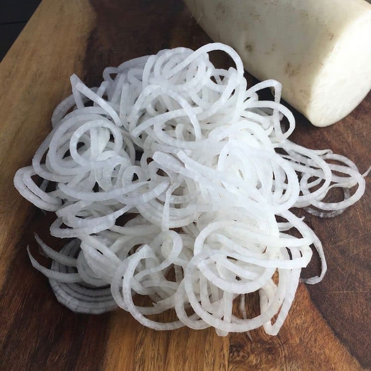 Spiralized daikon noodles piled on a wooden cutting board next to a whole daikon radish