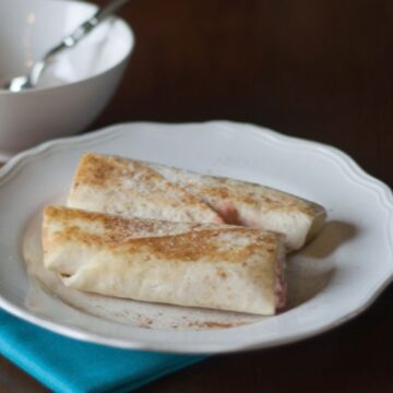 Tortilla cream cheese cinnamon roll-ups dusted with cinnamon sugar on a white plate