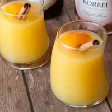 Two glasses of warm mulled mimosa cocktail garnished with cinnamon sticks and orange