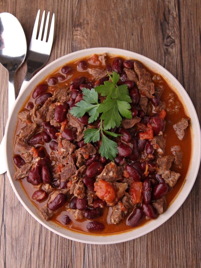 Overhead view of Weight Watchers chili with ground beef, kidney beans and tomatoes in a white bowl, topped with fresh parsley