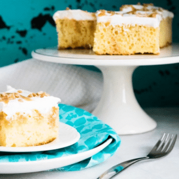 Caramel Toffee Poke Cake squares on a white cake stand with a slice on a plate