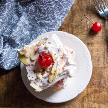 Slice of cherry almond poke cake with a maraschino cherry on a white plate