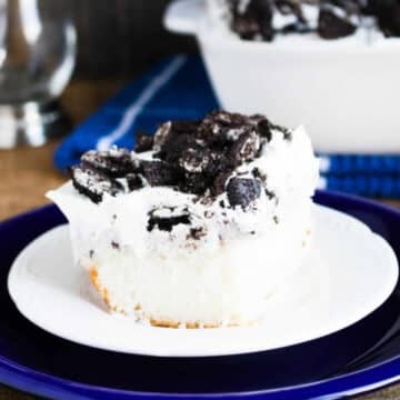 Slice of Oreo poke cake topped with whipped topping and crushed Oreos on a white plate