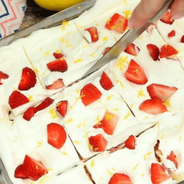 Strawberry poke cake topped with whipped topping, sliced fresh strawberries and lemon zest in a glass baking dish